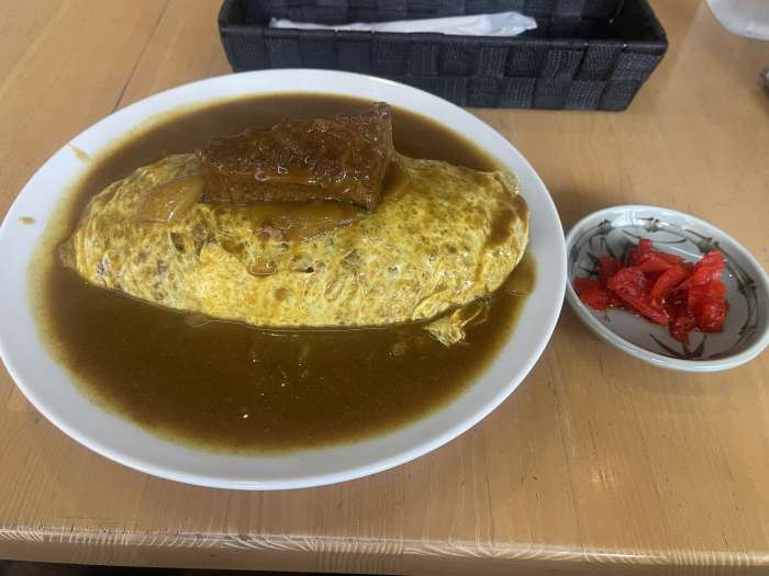 タブロースの名物オムカレー。薄焼き卵で包まれたご飯に角煮をトッピングし、福神漬けが添えられている